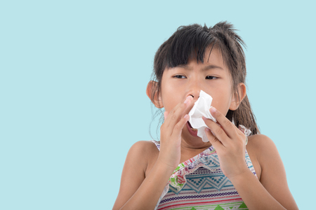 Flu cold or allergy symptom.Sick young asian girl with fever sneezing in tissue,allergies,the common cold,with blank copy space on blueの写真素材