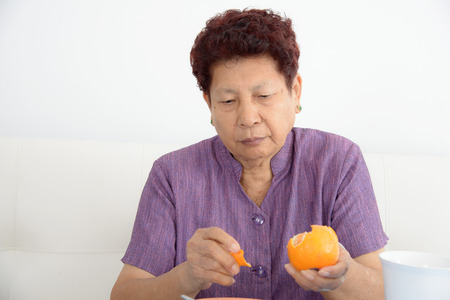 Serious Asian senior woman eating orange at home.の写真素材