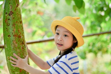 Cute Asian girl holding giant vegetable marrow from treeの写真素材