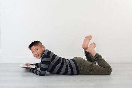 Boy lying on floor  and holding pad at home, copy space for textの写真素材