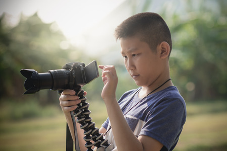Asian boy learning to taking photo from camera in his hand with nature outdoor background.の写真素材