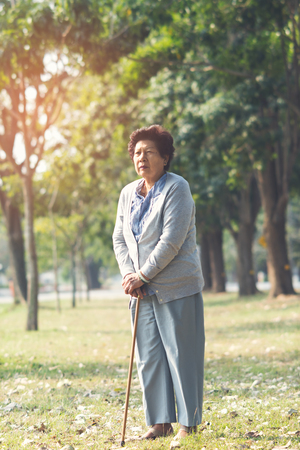 Asian senior woman with walking stick in nature background outdoor.の写真素材