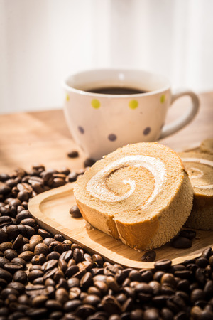 Roll coffee cake and coffee bean with wooden table and window lightの写真素材