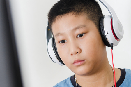 Asian boy wearing headphone while playing computer game at home.の写真素材