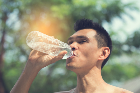 Sport man drinking a bottle of water with bokeh background outdoorの写真素材