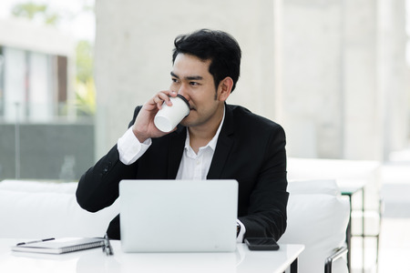 Asian businessman drinking coffee and work with laptop in cafe outside, lifestyle concept.の写真素材