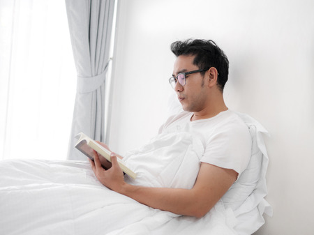 Happy Asian man reading a book on bed, man lifestyle on weekend concept.の写真素材