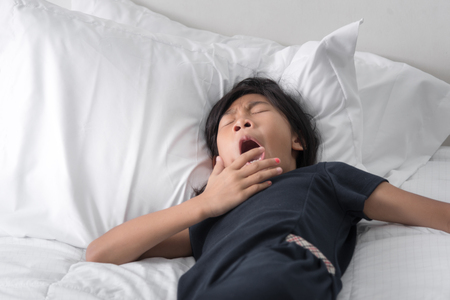 Yawning Asian girl sleeping on bed with copy space.の写真素材