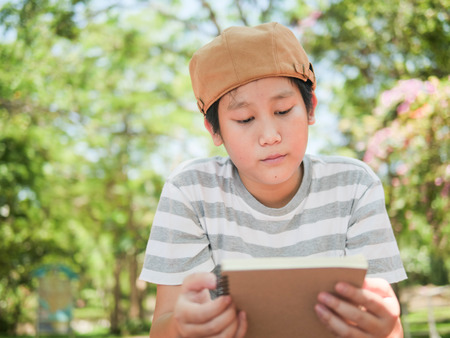 Happy Asian preteen boy reading a book outdoor.
