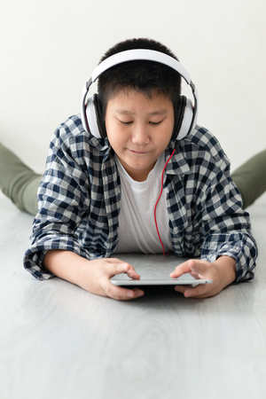 Happy Asian preteen boy lying on floor and using tablet and headphone.の写真素材
