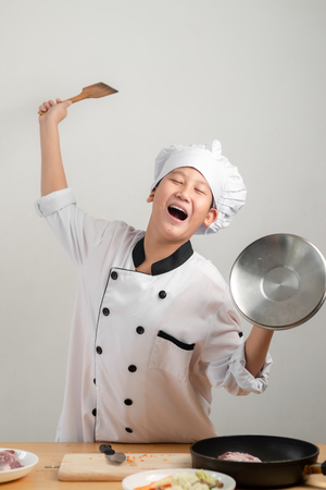 Funny Asian preteen chef holding spatula and pot lid for battle with food, lifestyle concept.の写真素材