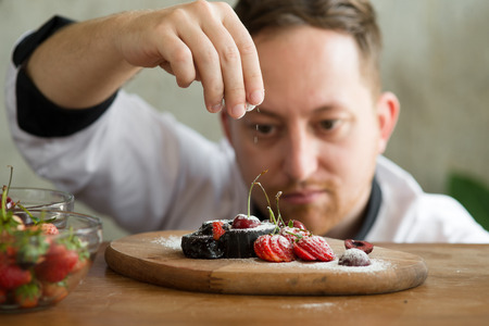Pastry chef spreading icing sugar on chocolate cake.の写真素材