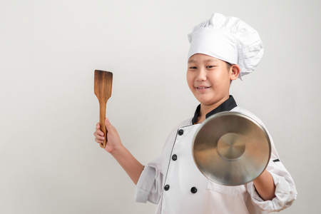 Funny Asian preteen chef holding spatula and pot lid for battle with food, lifestyle concept.の写真素材