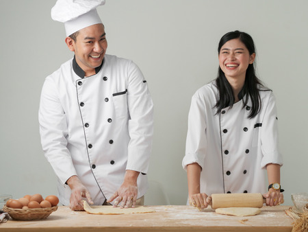 Laughing Asian chefs preparing dough for pizza or bread on table, work lifestyle concept.