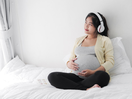 Asian pragnant woman using headphone listening music on bed, lifestyle concept.の写真素材
