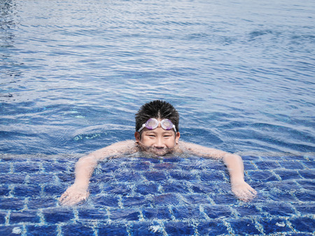 Asian boy wearing goggles and swimming in pool in sunny day.の写真素材