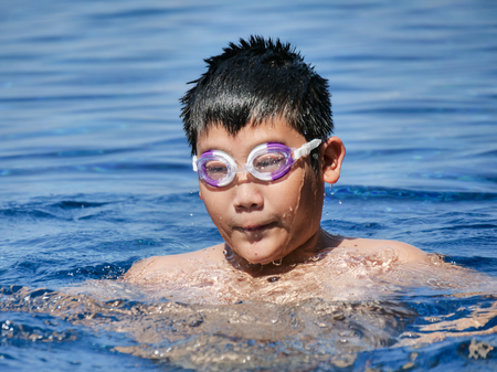 Asian boy wearing goggles and swimming in pool in sunny day.の写真素材