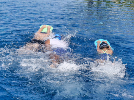 Children learning to swimming on foam board with their coach in pool in sunny day.