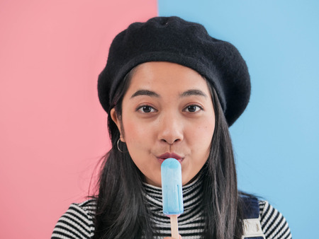 Happy Asian woman eating blue ice cream stick with color background.