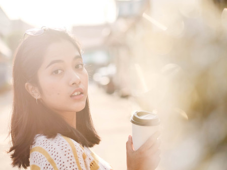 Happy Asian woman holding a plastic coffee cup outdoor with sun light in winter.