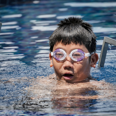 Asian boy wearing goggles and swimming in pool in sunny day.