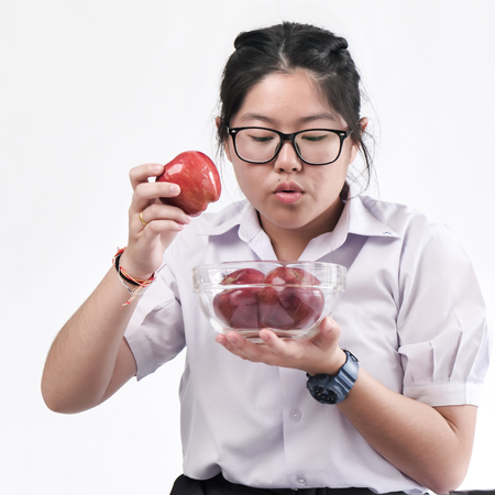 Asian schoolgirl in Thai uniform holding red apples in bowl on white background.の写真素材