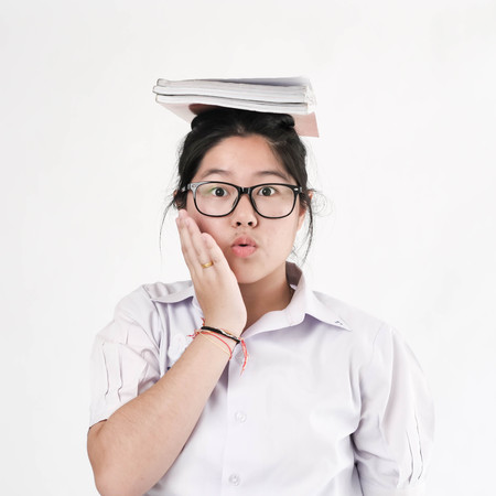 Happy Asian student in uniform putting books stack on her head, education concept.