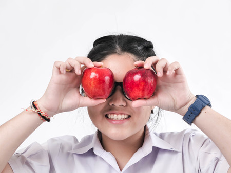 Happy schoolgirl hiding her eyes with red apple, lifestyle concept.の写真素材