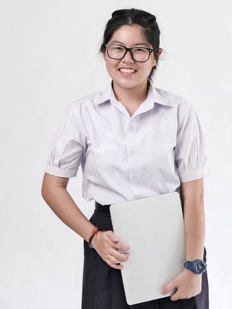 Happy Asian student in uniform holding laptop on white background.の写真素材