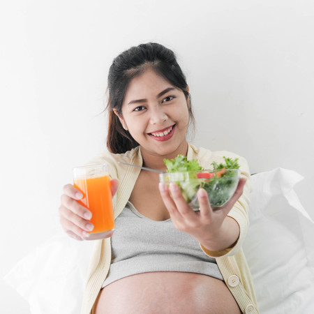 Asian pregnant woman showing eating fruit salad and a glass of orange juice in her hands, lifestyle concept.の写真素材