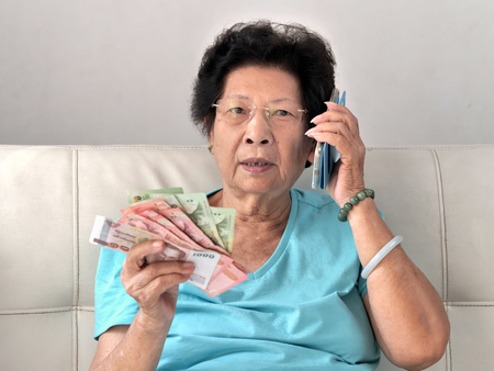 Asian senior woman holding Thai Baht money while talking a phone call, lifestyle concept.