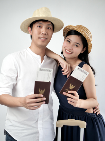 Happy Asian tourist couple holding Thailand passport and suitcase on gray background.の写真素材