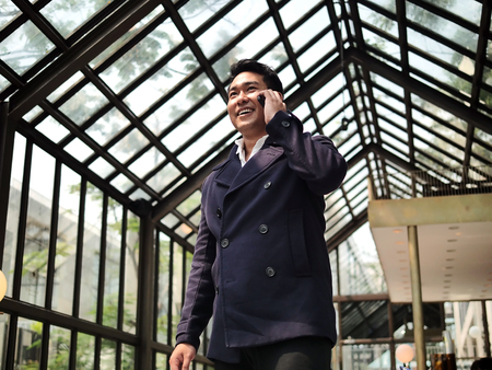 Happy Asian businessman in blue coat talking phone in cafe, lifestyle concept.の写真素材