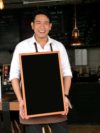 Asian barista man holding blank black board in front of coffee shop.の写真素材