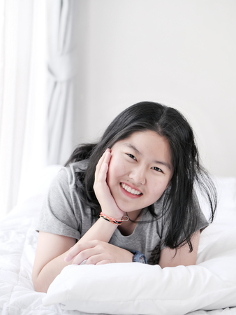 Happy Asian teenager lying on bed and looking at camera, lifestyle concept.の写真素材