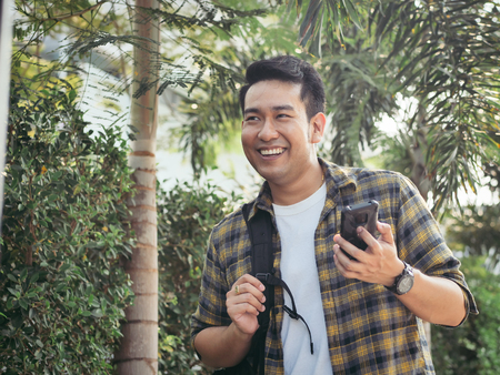Happy Asian man with backpack holding smartphone, lifestyle concept.の写真素材