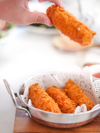 Hand holding fried cheese sticks in aluminium pan on wooden table, ready to eat.の写真素材