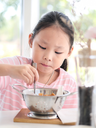 Asian girl eating fried sausages in the aluminium bowl near window at home.の写真素材