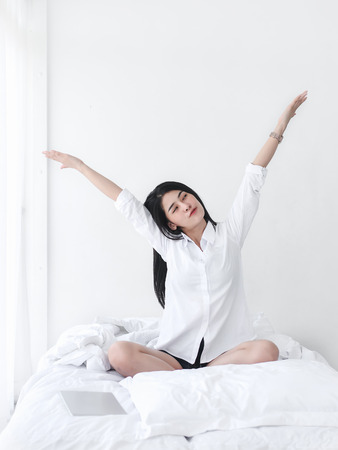 Attractive Asian girl sitting on white bed and relax at home.の写真素材
