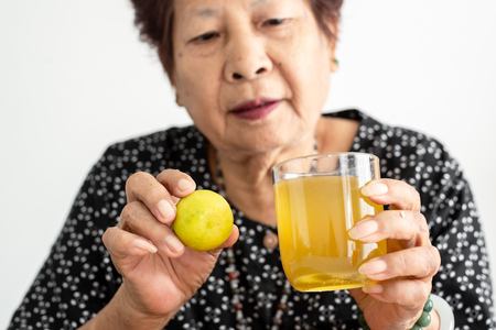 Asian senior woman holding lemon and honey juice in glass at home, lifestyle concept.の写真素材