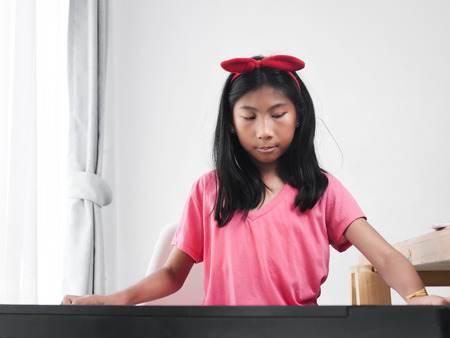 Asian girl playing keyboard piano near window at home.の写真素材