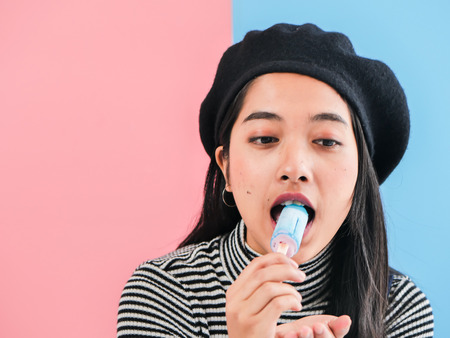 Happy Asian woman eating blue ice cream stick with color background.の写真素材