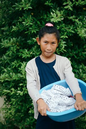 Asian girl holding blue clothes basin with green tree background, lifestyle concept.の写真素材