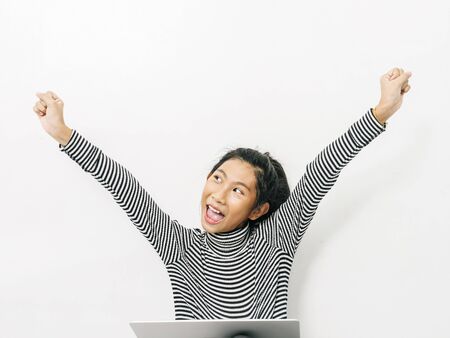 Asian girl sitting on floor and using laptop, raising hands at home.の写真素材