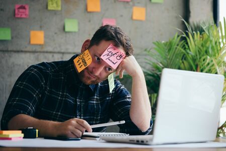 Stressed man with message on sticky notes over his face in office.
