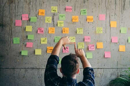 Back of entrepreneur sitting in office and look at colorful sticky message on cement wall. Work...