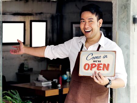 Cheerful Asian barista man holding welcome board in front of coffee shop.の写真素材