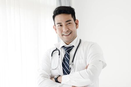 Confident Asian doctor with arms crossed near window, lifestyle concept.の写真素材