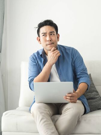 Stressed Asian man using laptop at home, lifestyle concept with copy space.の写真素材