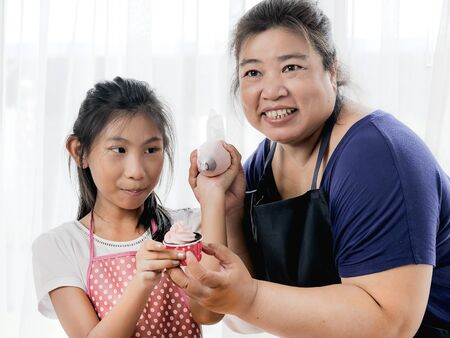 Asian girl learning with her mother preparing for decorate homemade cupcake, lifestyle concept.